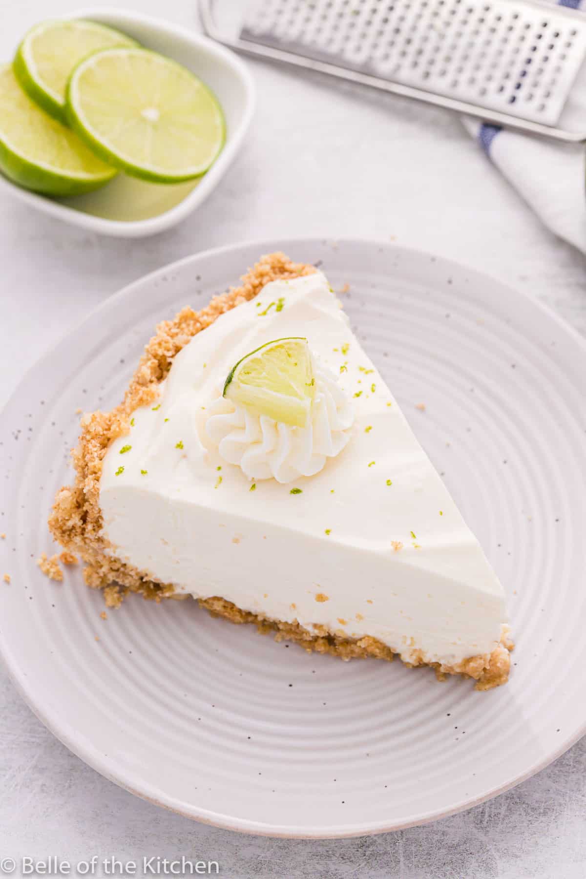 a slice of pie on a white plate topped with whipped cream and limes.