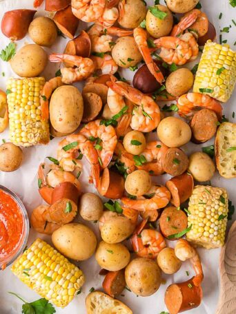 shrimp, corn, potatoes and sausage spread on a table next to a bowl of cocktail sauce.