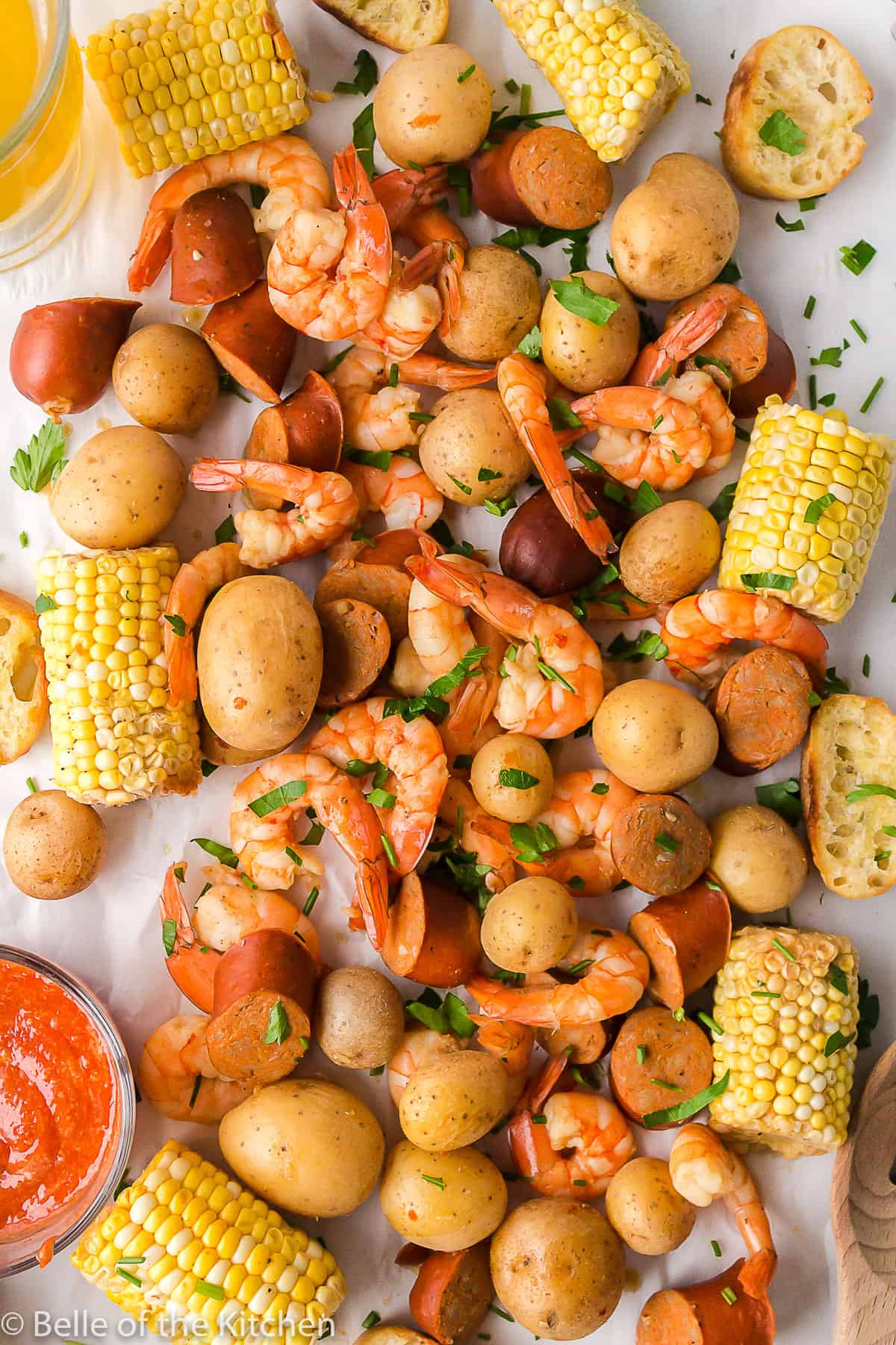 shrimp, corn, potatoes and sausage spread on a table next to a bowl of cocktail sauce.