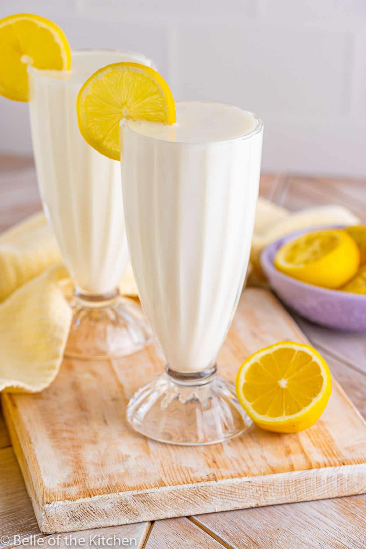 two glasses full of lemon milkshake with lemon slices on the side.