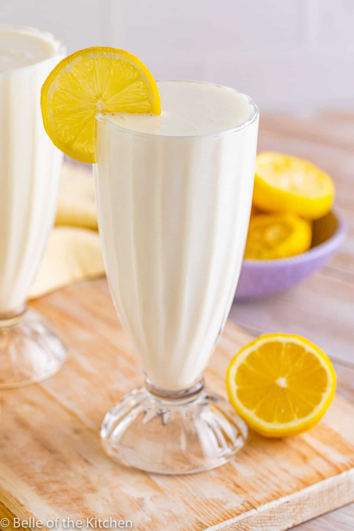 a lemon milkshake in a glass on a wooden cutting board.
