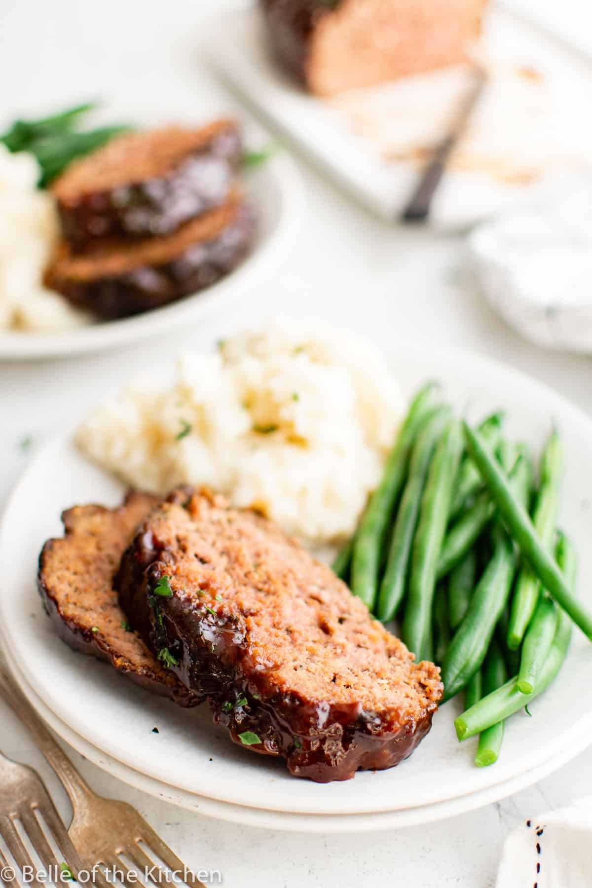 two slices of meatloaf on a plate with mashed potatoes and green beans.