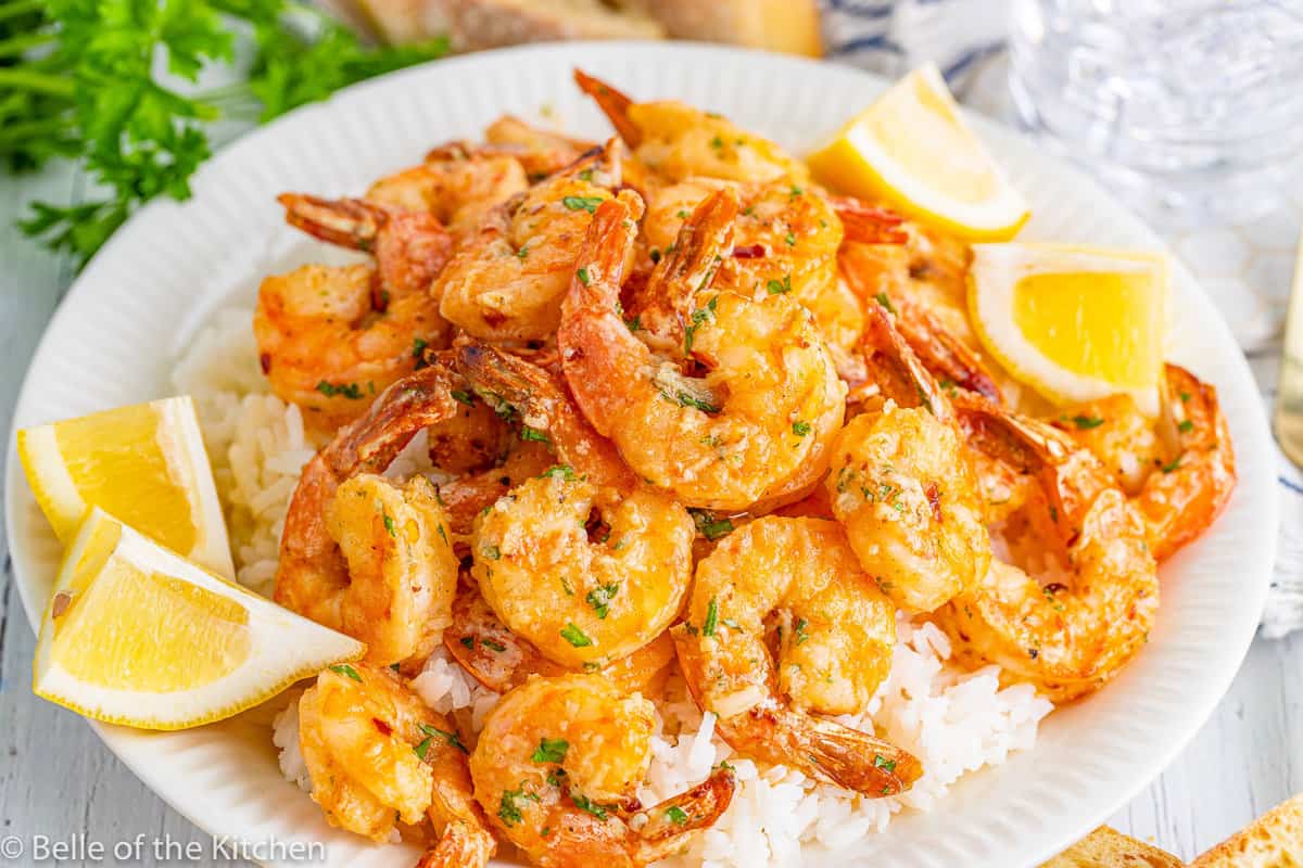 a plate full of rice and shrimp with lemon on the side.