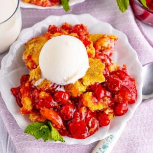 a plate of cherry cobbler with vanilla ice cream on top.