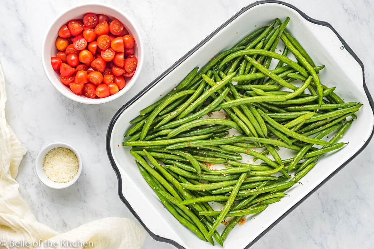 a baking pan of green beans next to a bowl of tomatoes.