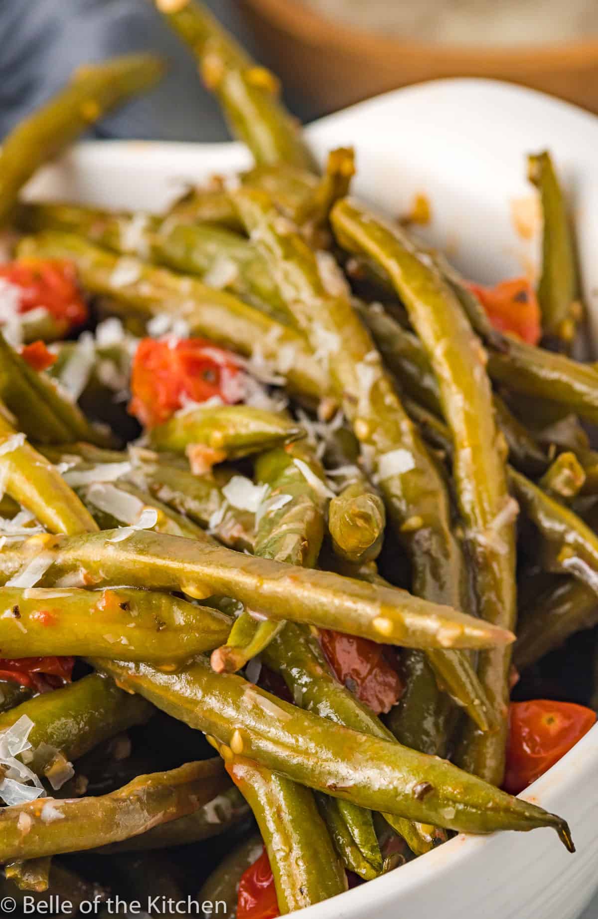 a bowl of green beans with tomatoes and cheese.