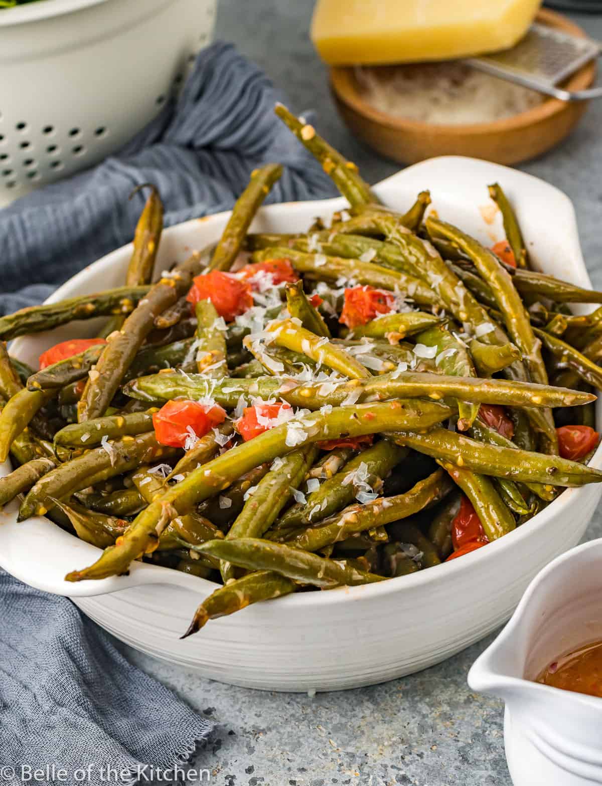 a bowl of green beans with tomatoes and cheese.