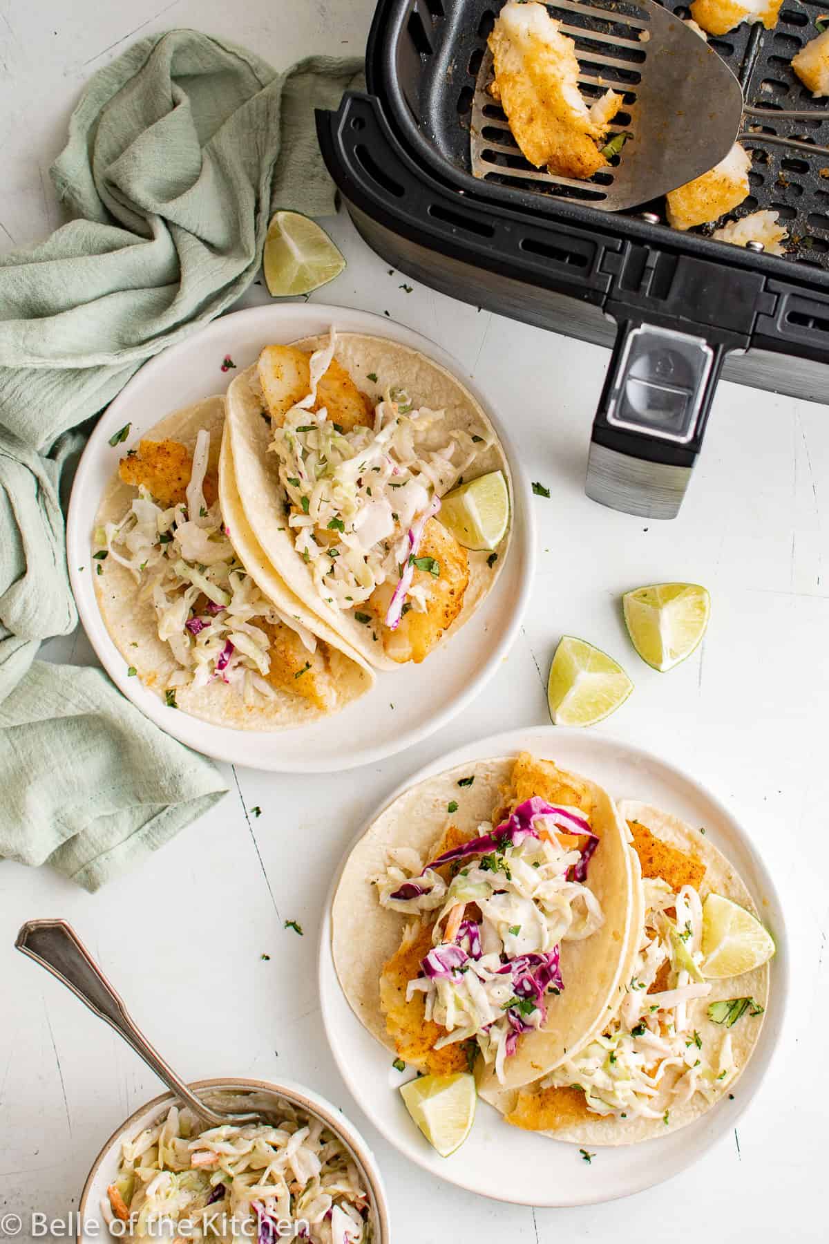fish tacos on plates next to an air fryer basket.