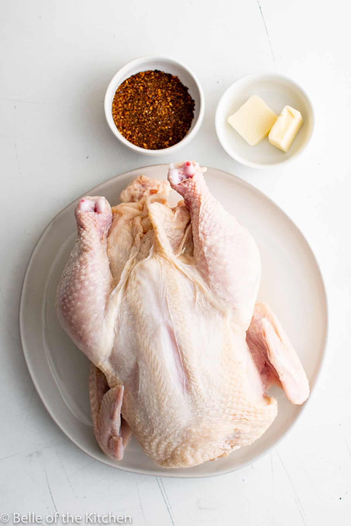 a whole raw chicken on a plate next to seasoning and butter.