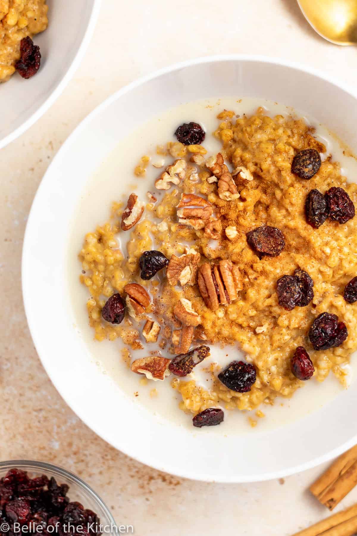 a white bowl of pumpkin oatmeal with raisin and pecans.