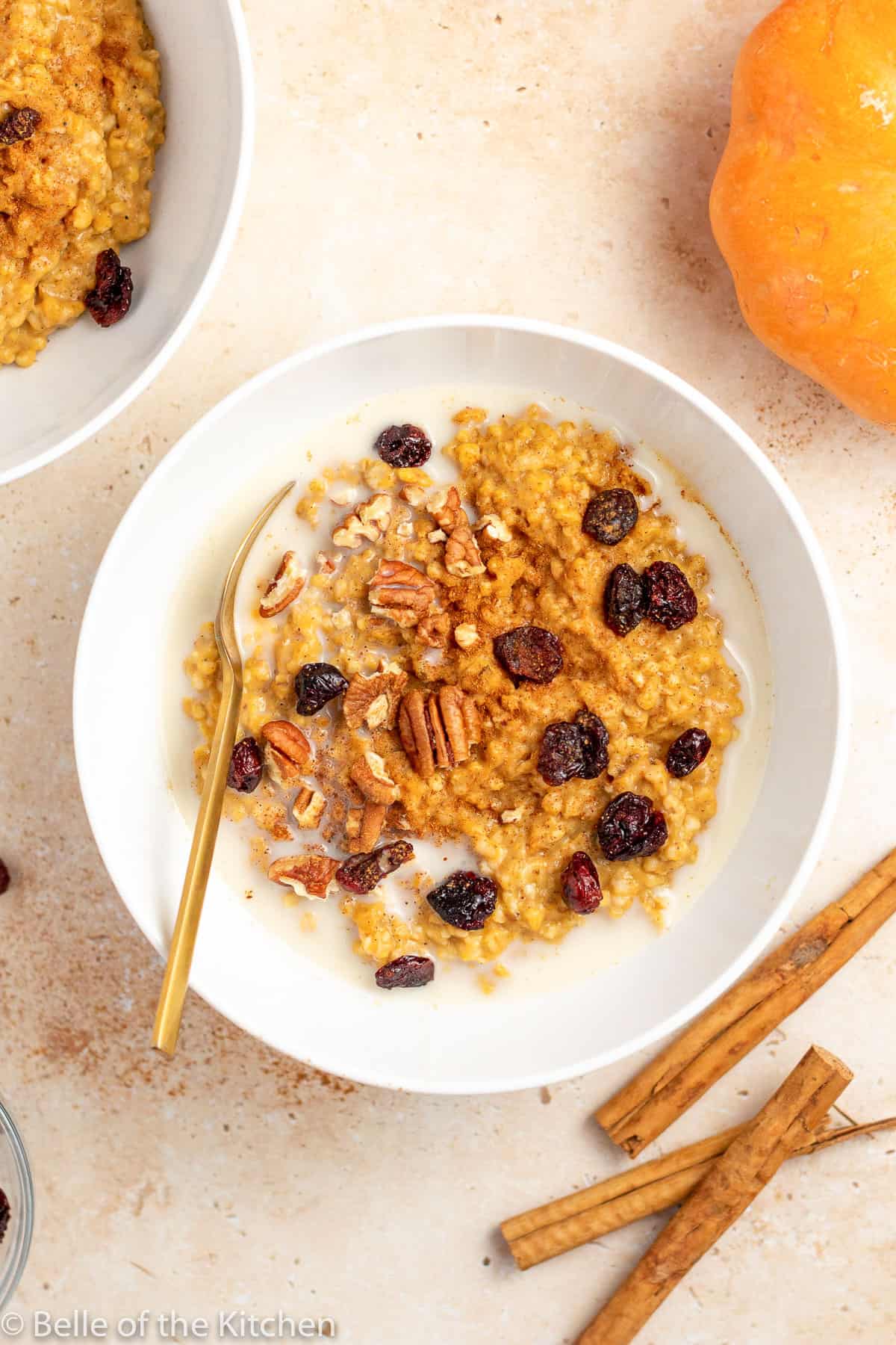 a white bowl of pumpkin oatmeal with raisin and pecans.