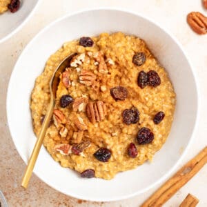 a bowl of pumpkin spice oatmeal topped with raisins and pecans.