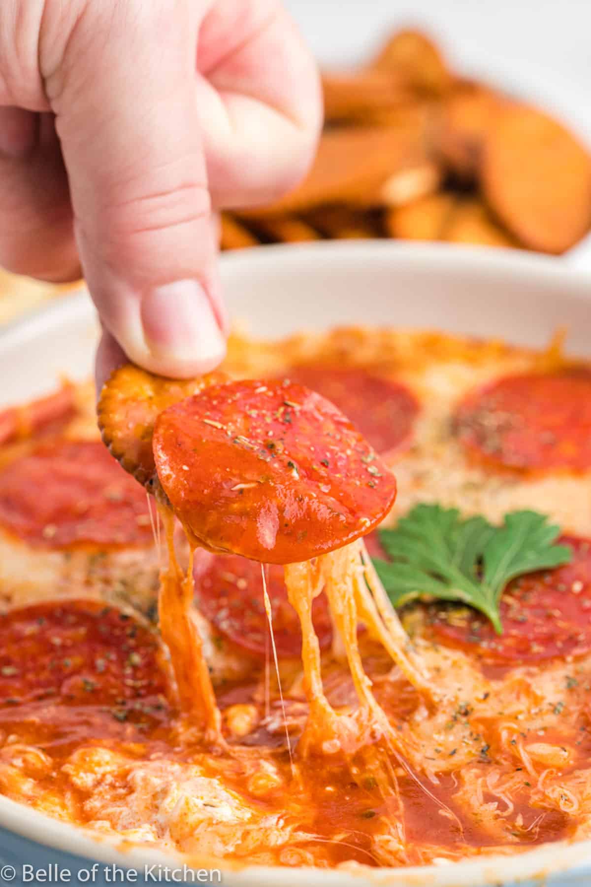 a piece of pepperoni being lifted with a cracker.