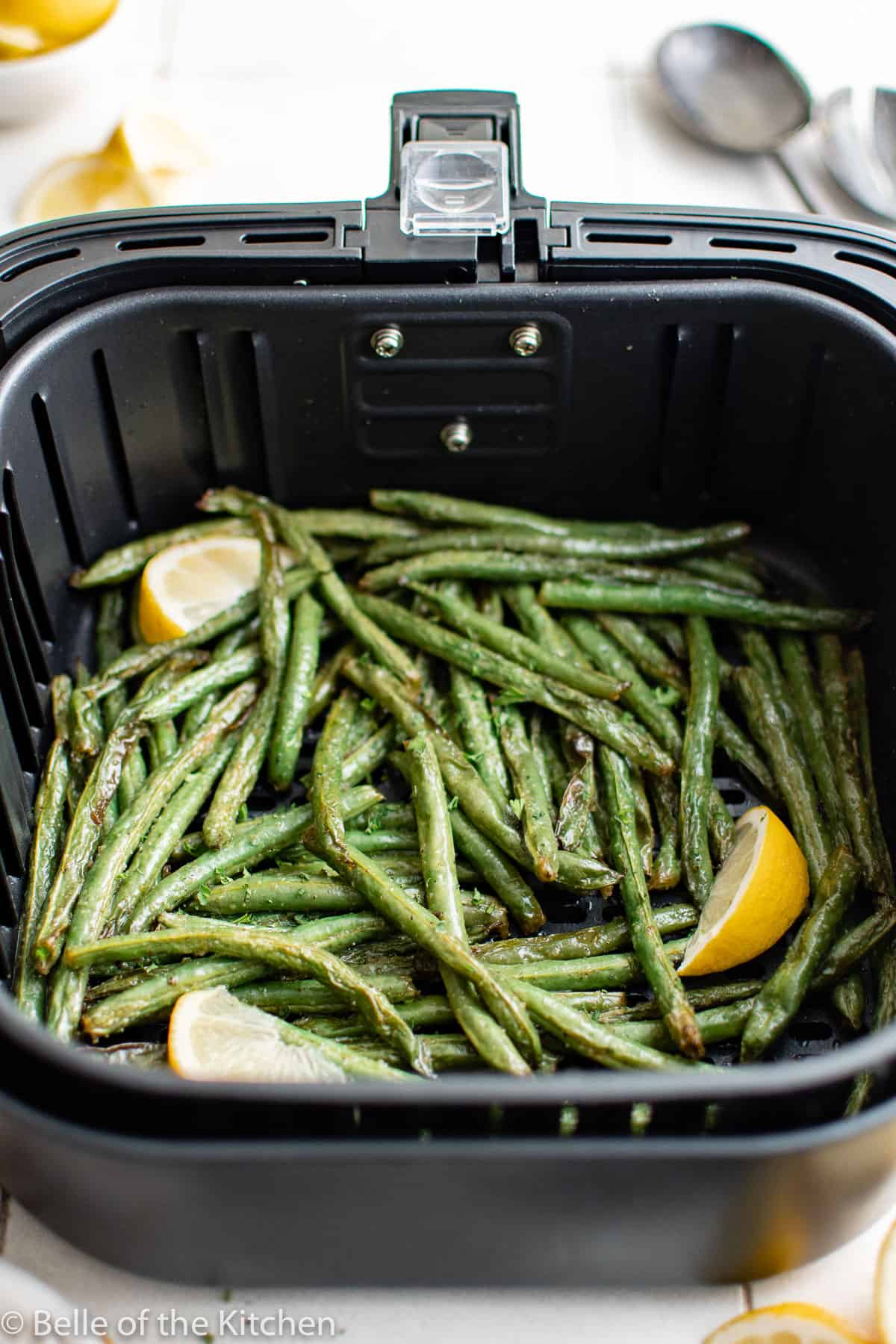 an air fryer basket full of green beans with lemon slices.