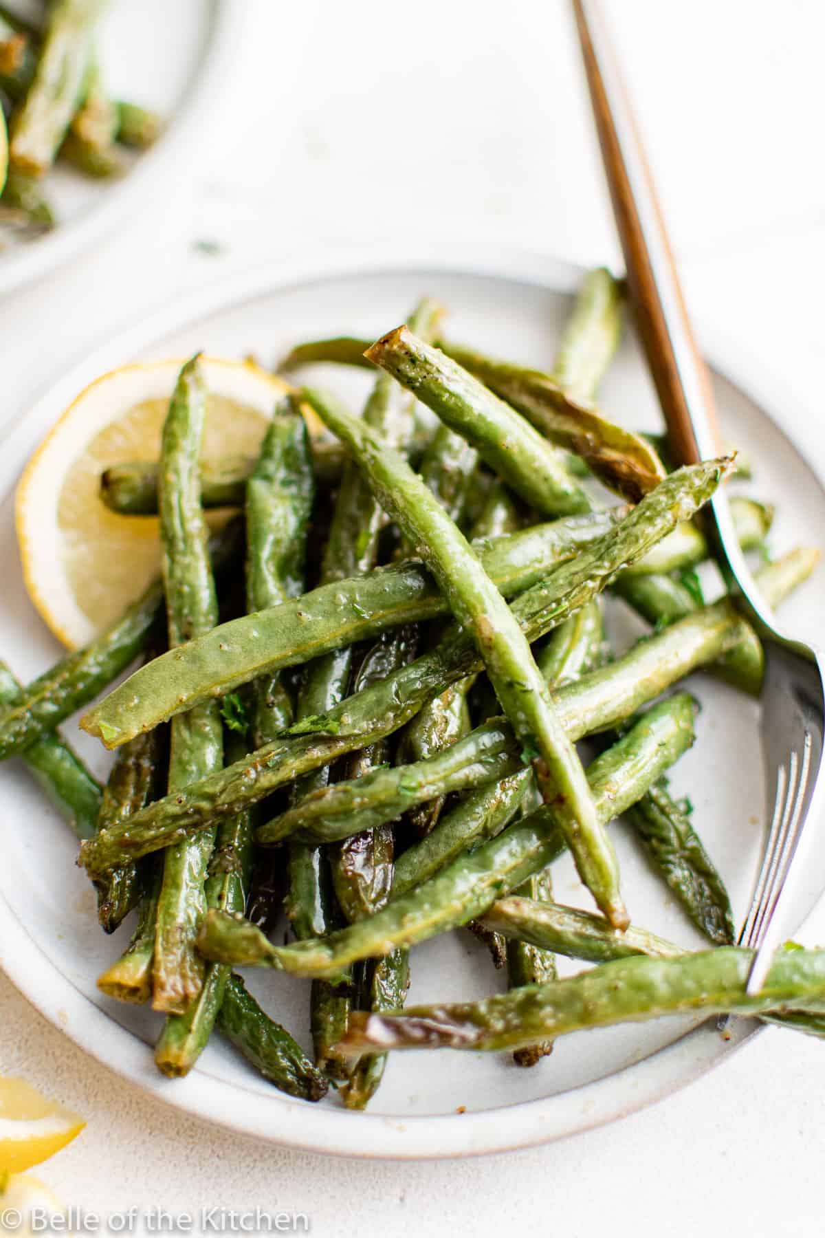 a white plate full of green beans with a fork.
