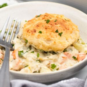 chicken and vegetables in a bowl topped with a biscuit and fork.