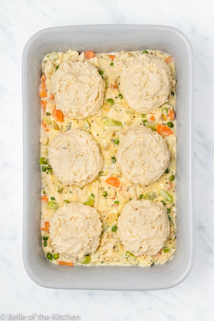 a baking dish full of chicken, vegetables, and biscuits.