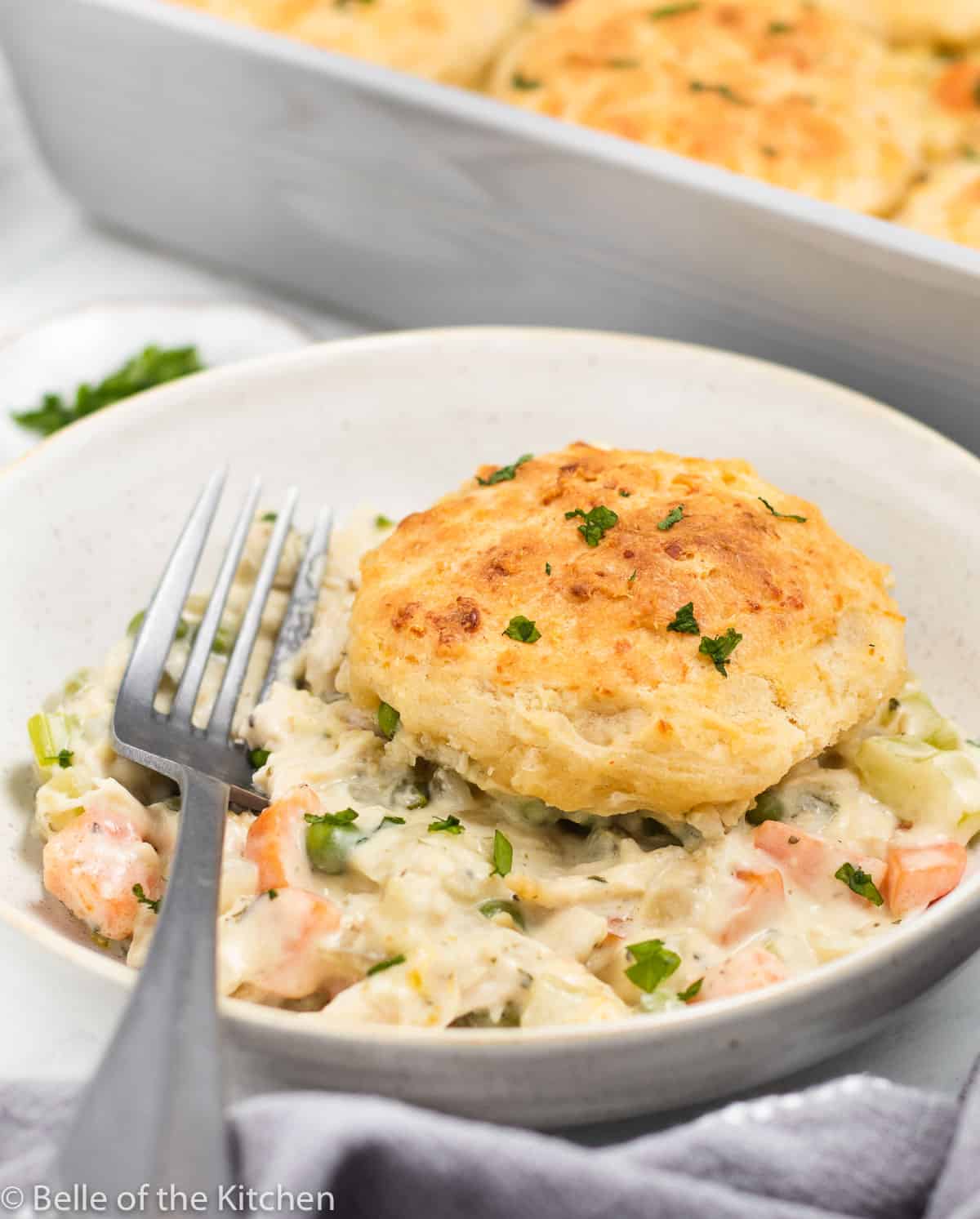 chicken and vegetables in a bowl topped with a biscuit and fork.
