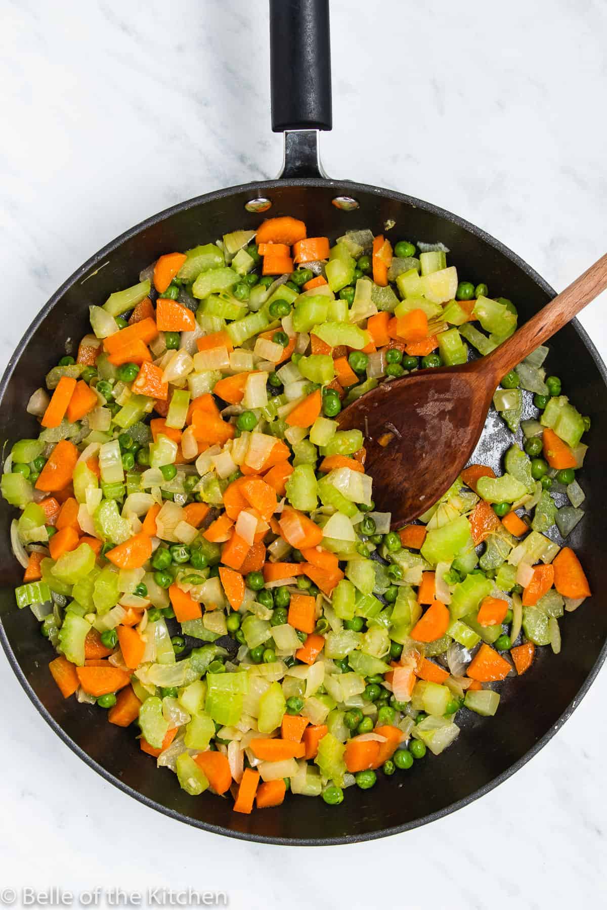a skillet full of vegetables and a wooden spoon.