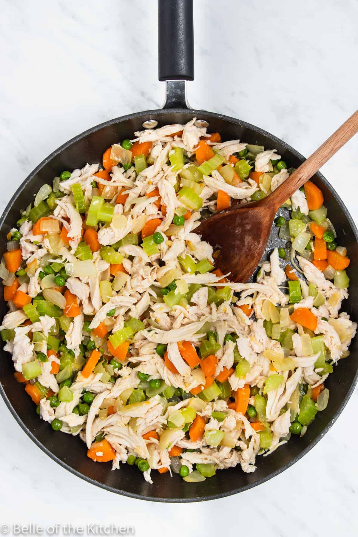 a skillet full of vegetables, chicken, and a wooden spoon.