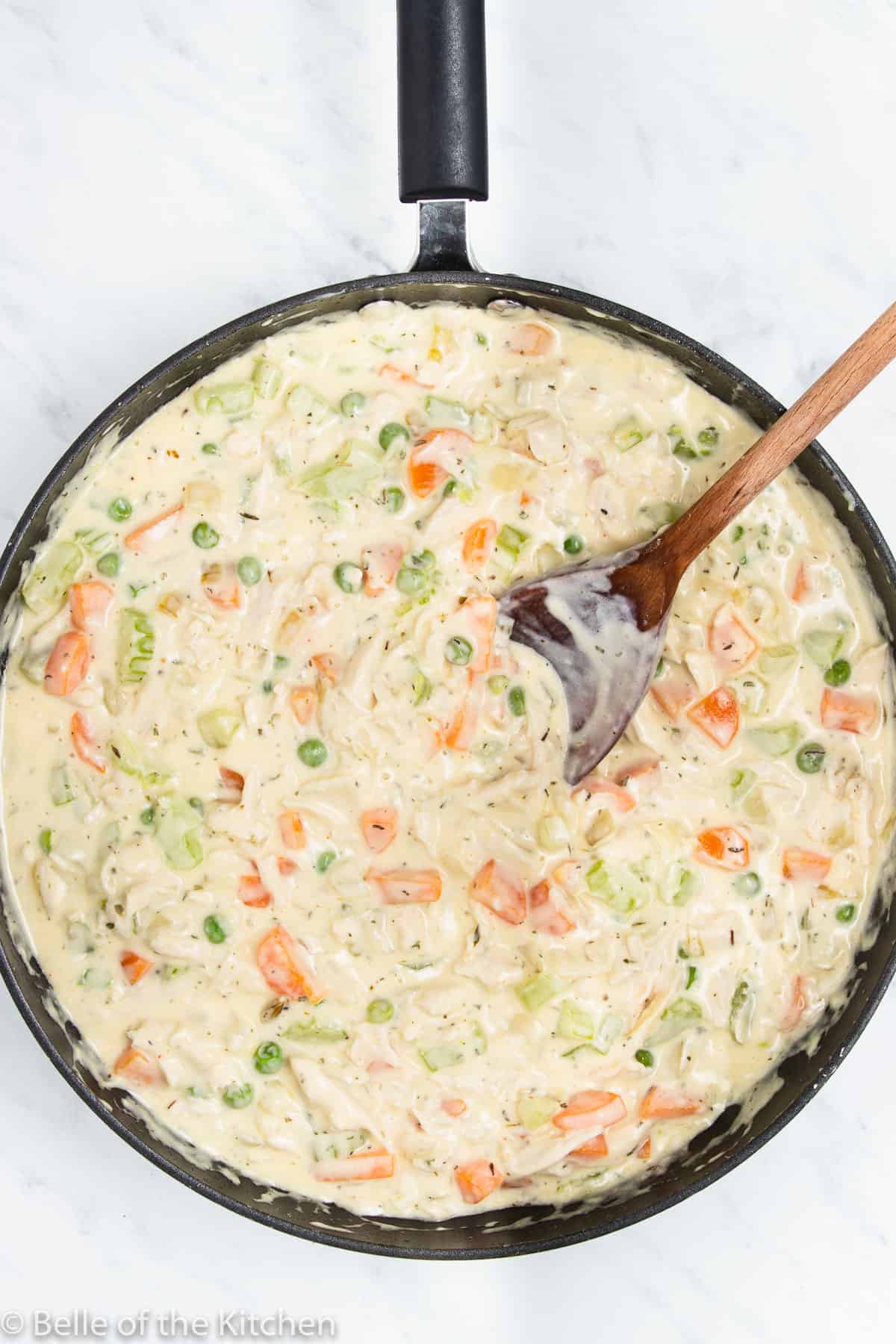 a skillet full of vegetables, creamy chicken, and a wooden spoon.