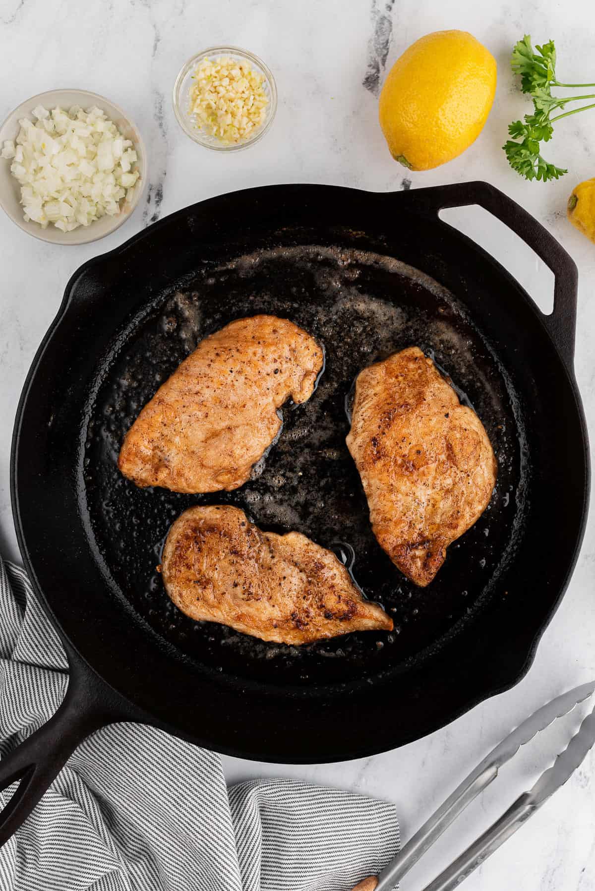 chicken breasts cooking in a black skillet.
