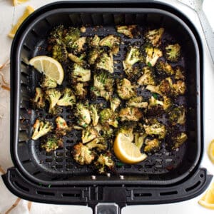 an air fryer basket fall of broccoli and lemon slices.