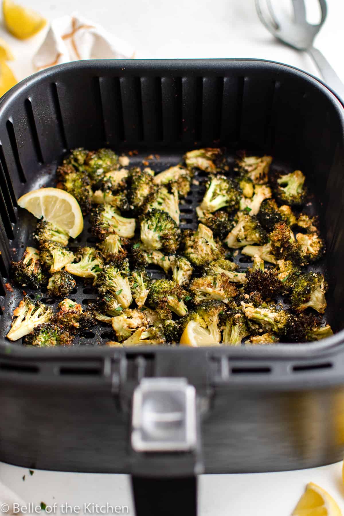 an air fryer basket fall of broccoli and lemon slices.