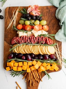a charcuterie board of cheese, grapes, olives, tomatoes, and salami in the shape of a Christmas tree.