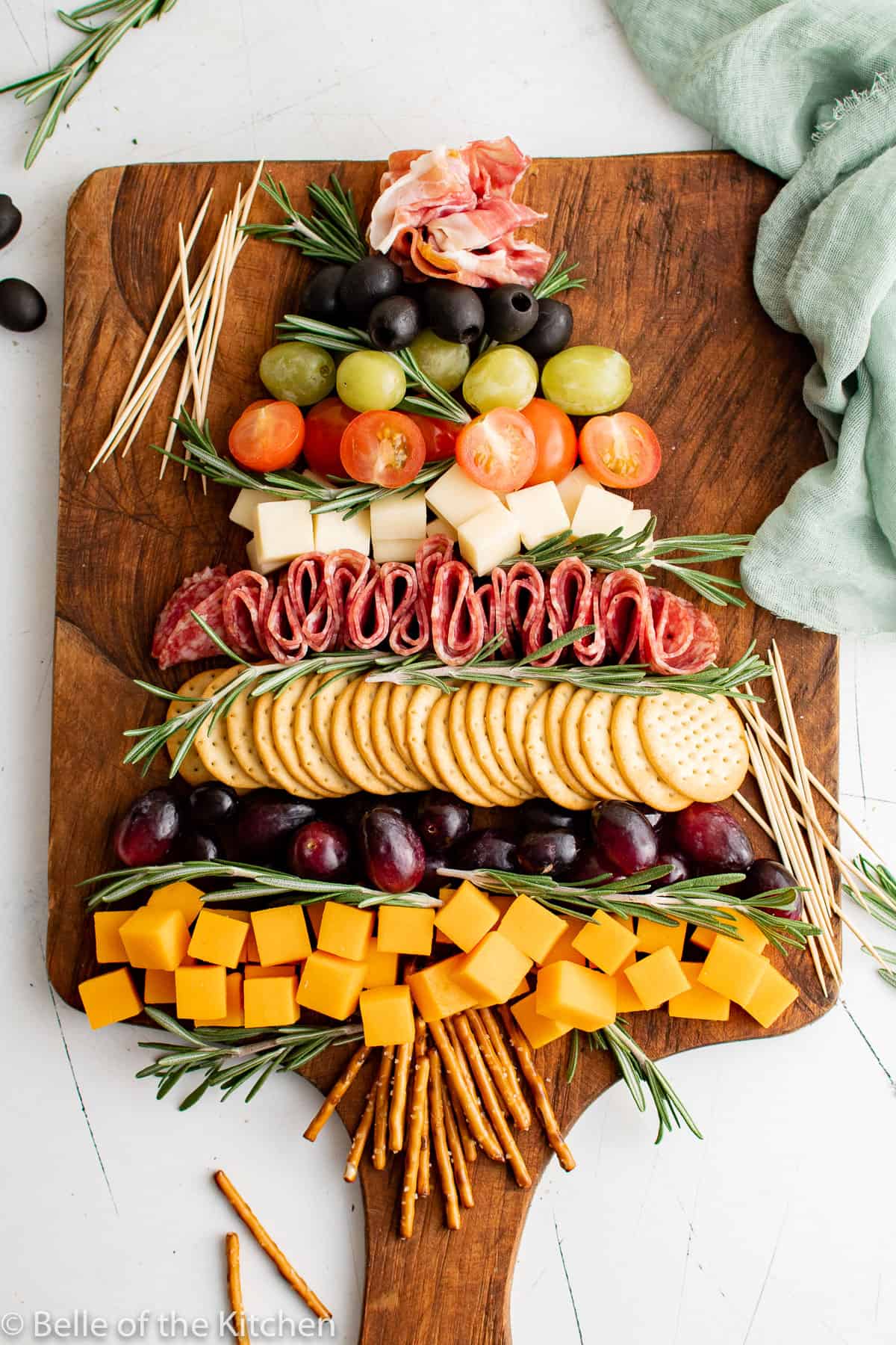 a charcuterie board of cheese, grapes, olives, tomatoes, and salami in the shape of a Christmas tree. 