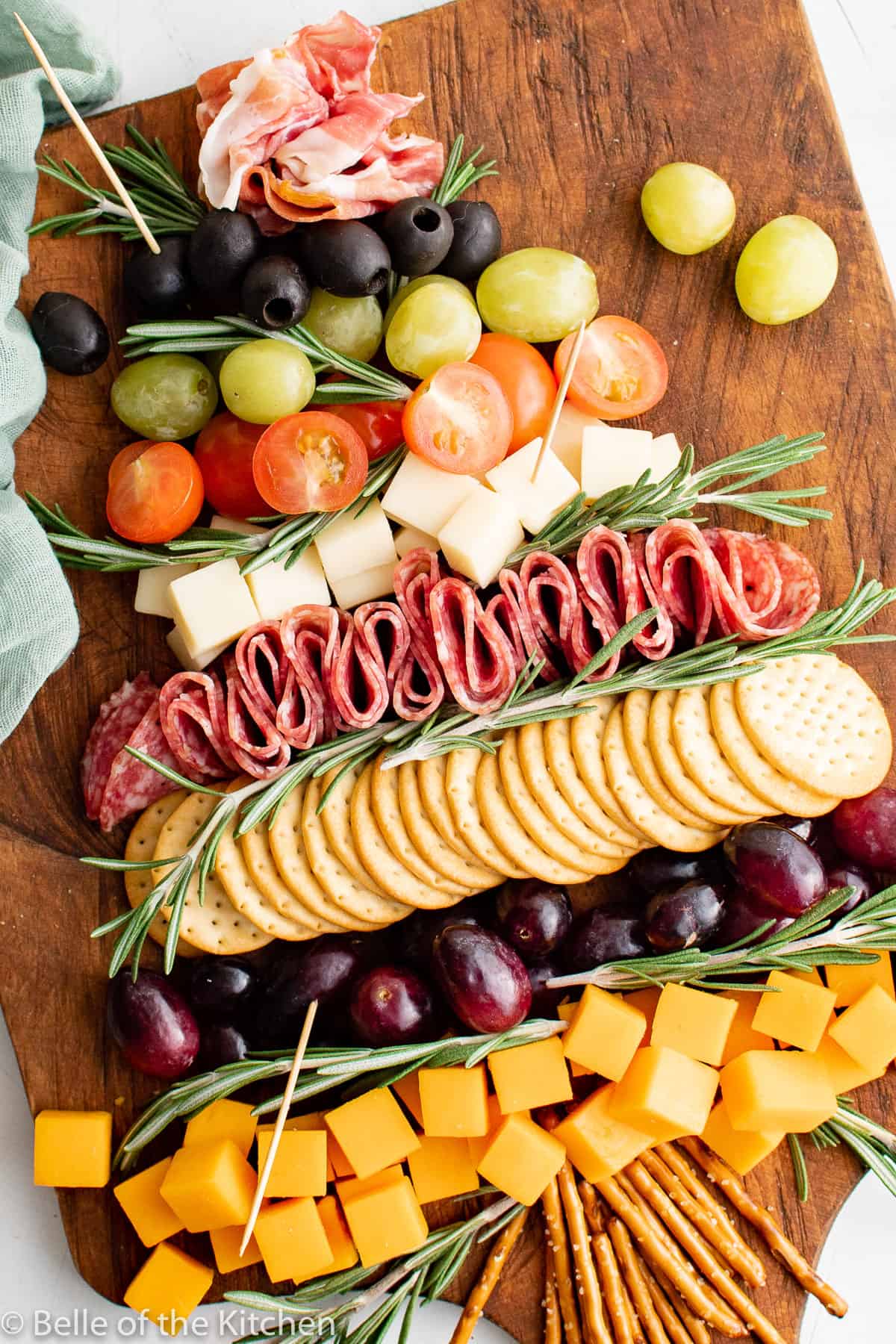a charcuterie board of cheese, grapes, olives, tomatoes, and salami in the shape of a Christmas tree.