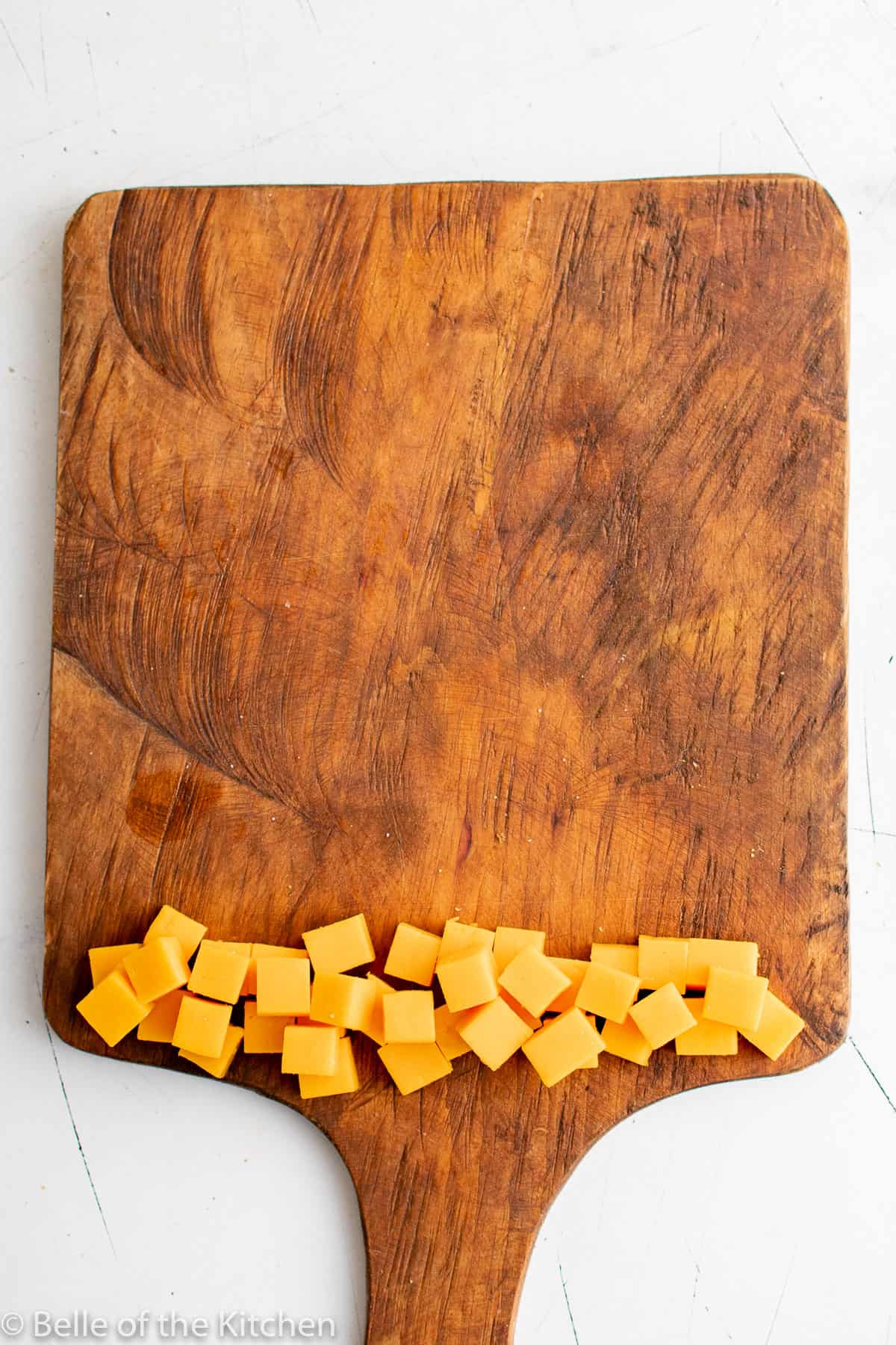 cut up cheese cubes on a wooden cutting board.
