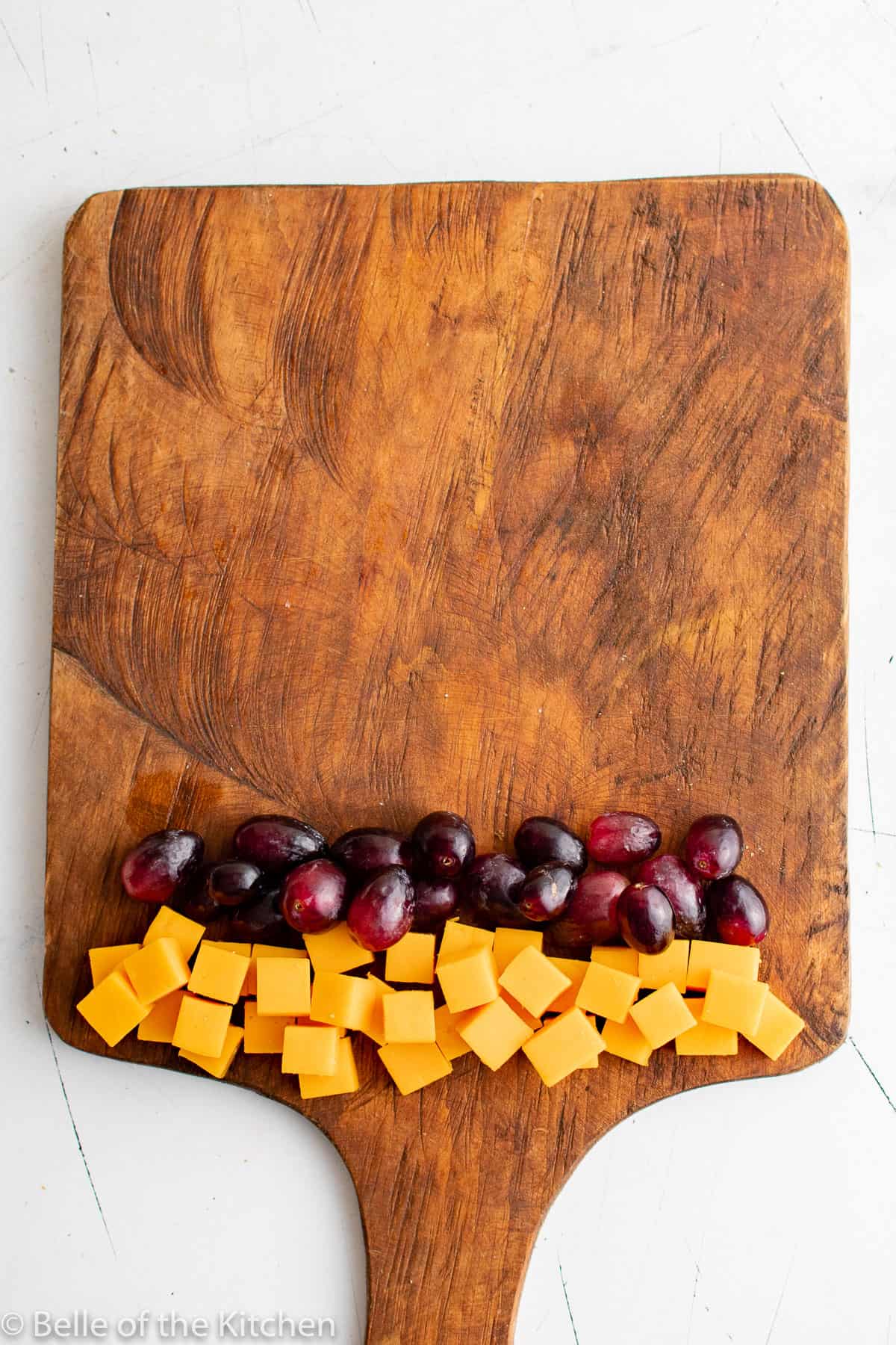 cut up cheese cubes and grapes on a wooden cutting board.