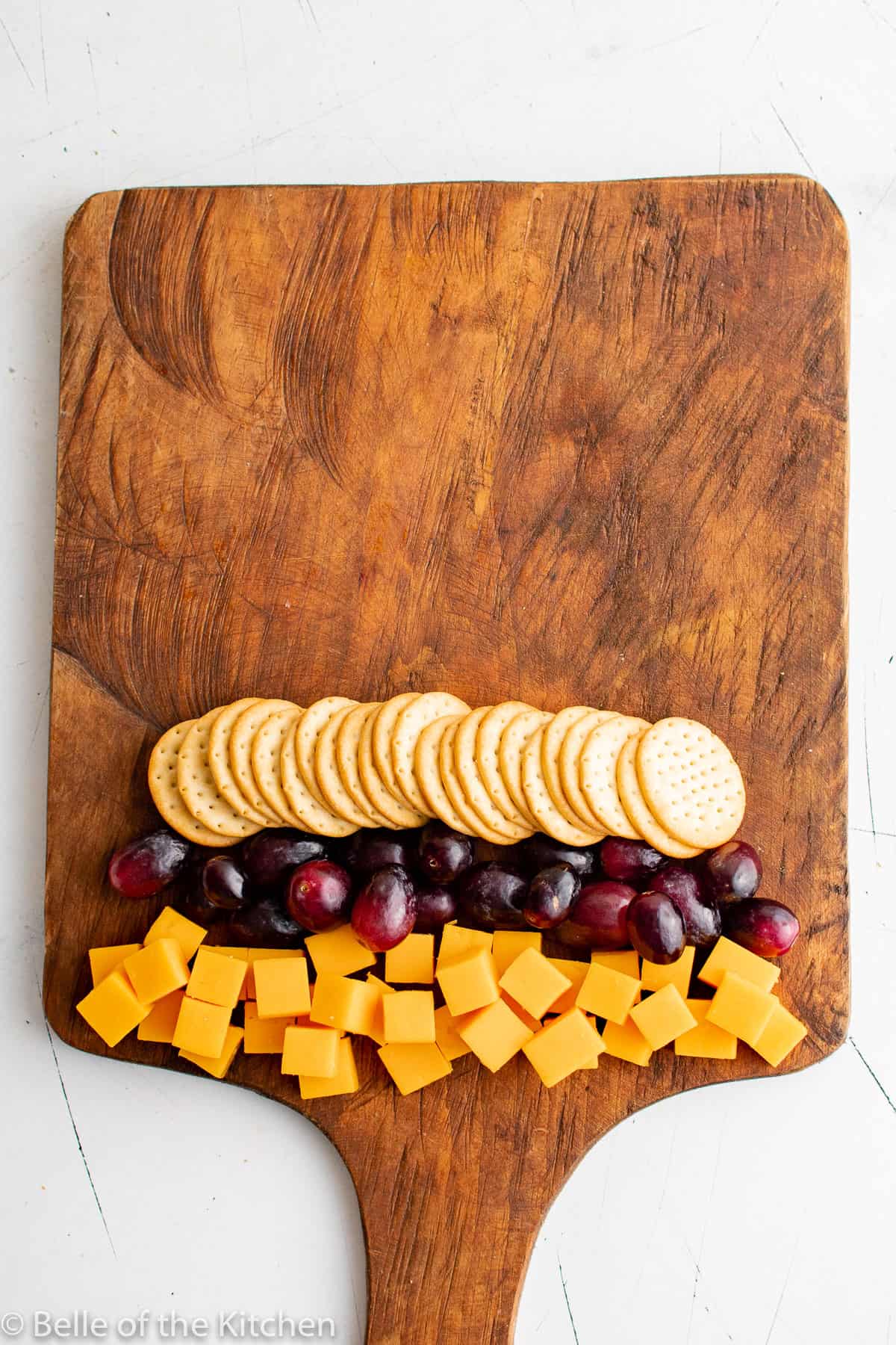 cut up cheese cubes, grapes, and crackers on a wooden cutting board.