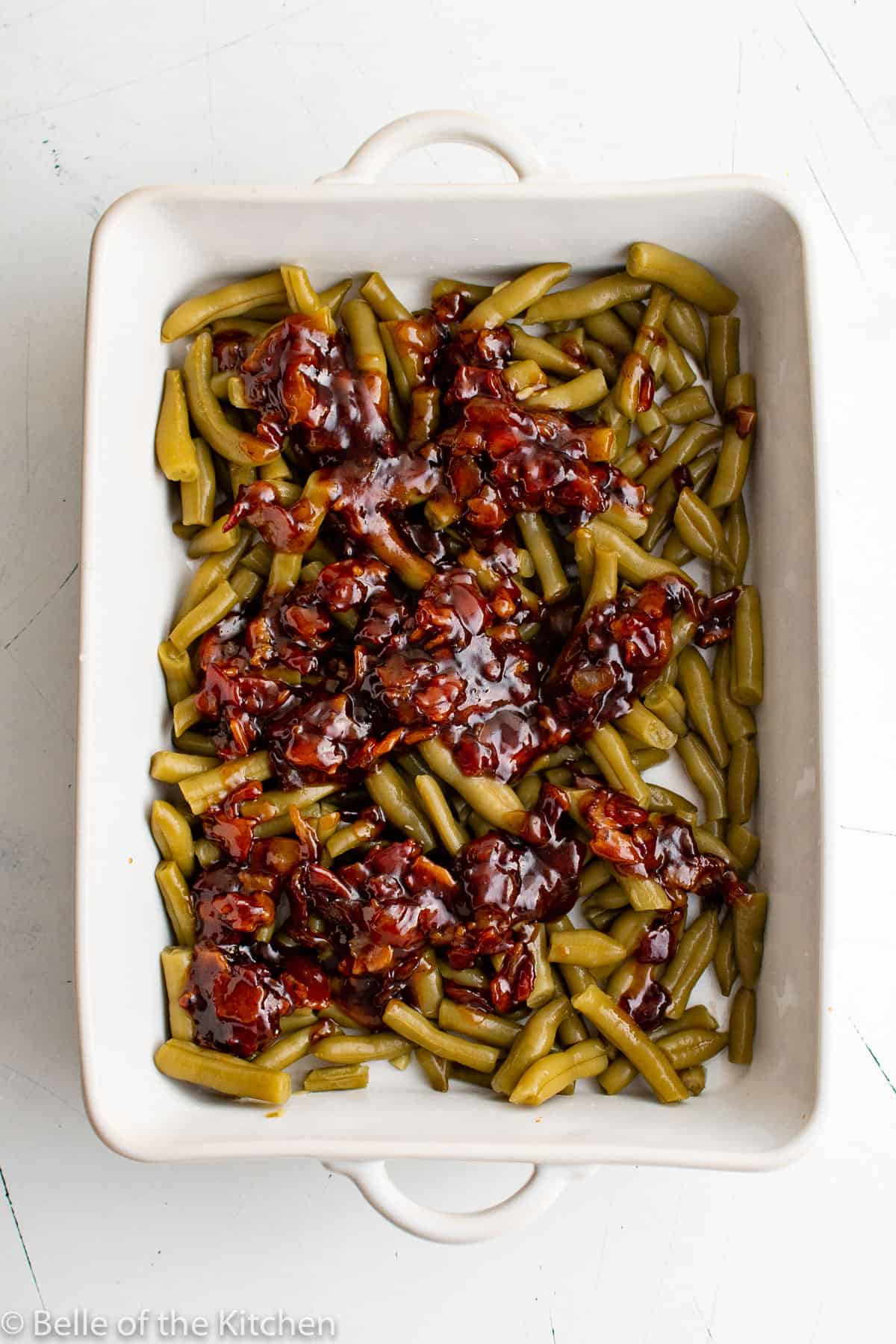 a white baking dish full of green beans and sauce.