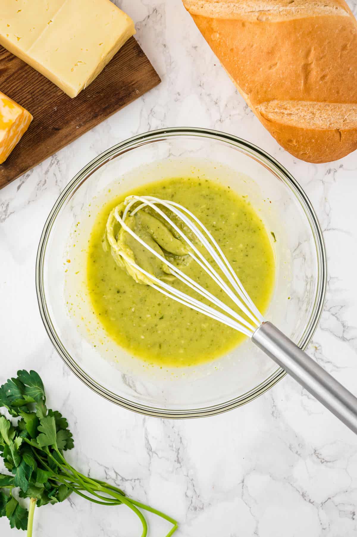 a glass bowl full of pesto, butter, and garlic with a whisk.