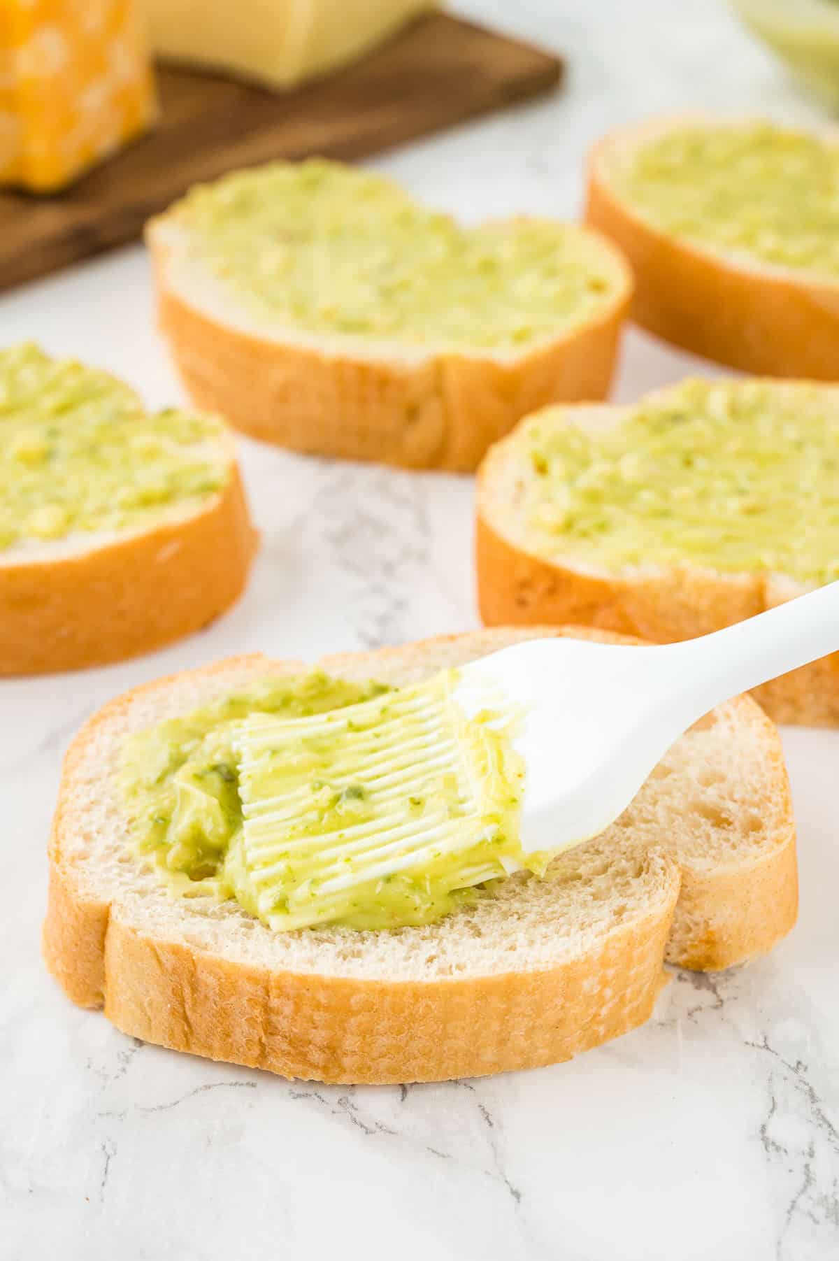 a spatula brush rubbing garlic butter onto bread slices.