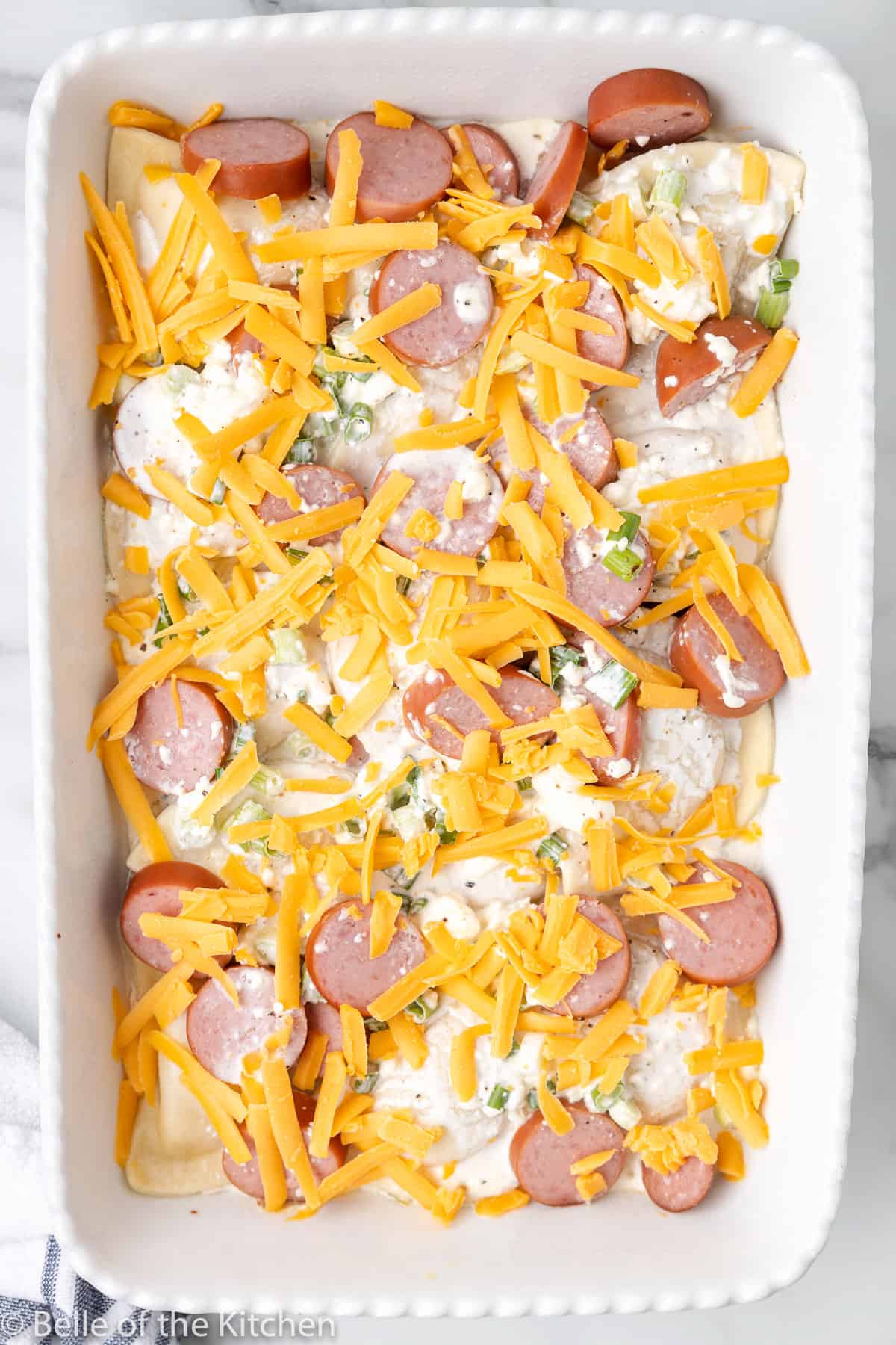 a casserole dish full of pierogies, sausage, cheese, and green onions.