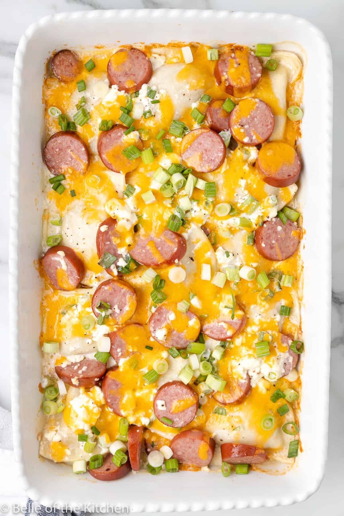a casserole dish full of pierogies, sausage, cheese, and green onions.