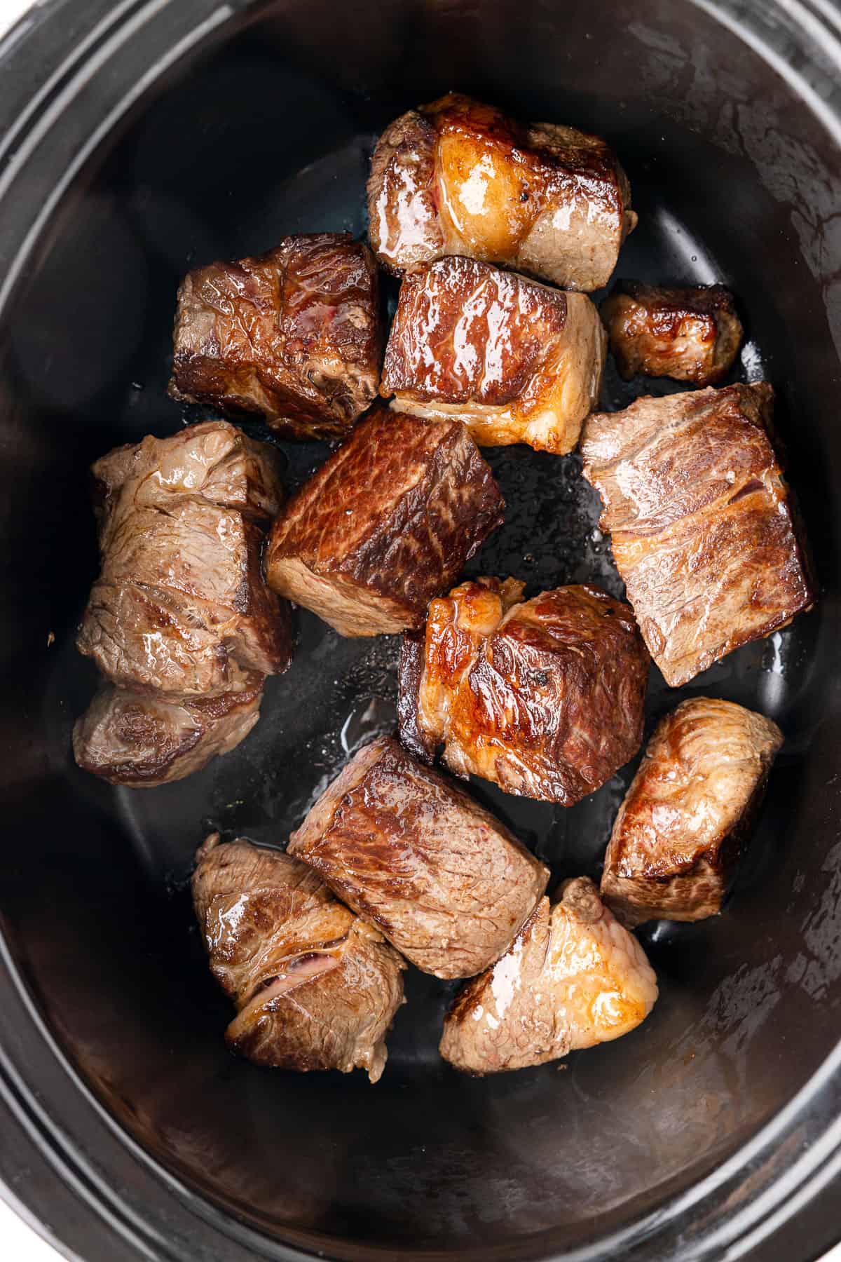 pieces of seared beef in a crockpot.