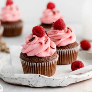 cupcakes on a plate with raspberries on top.