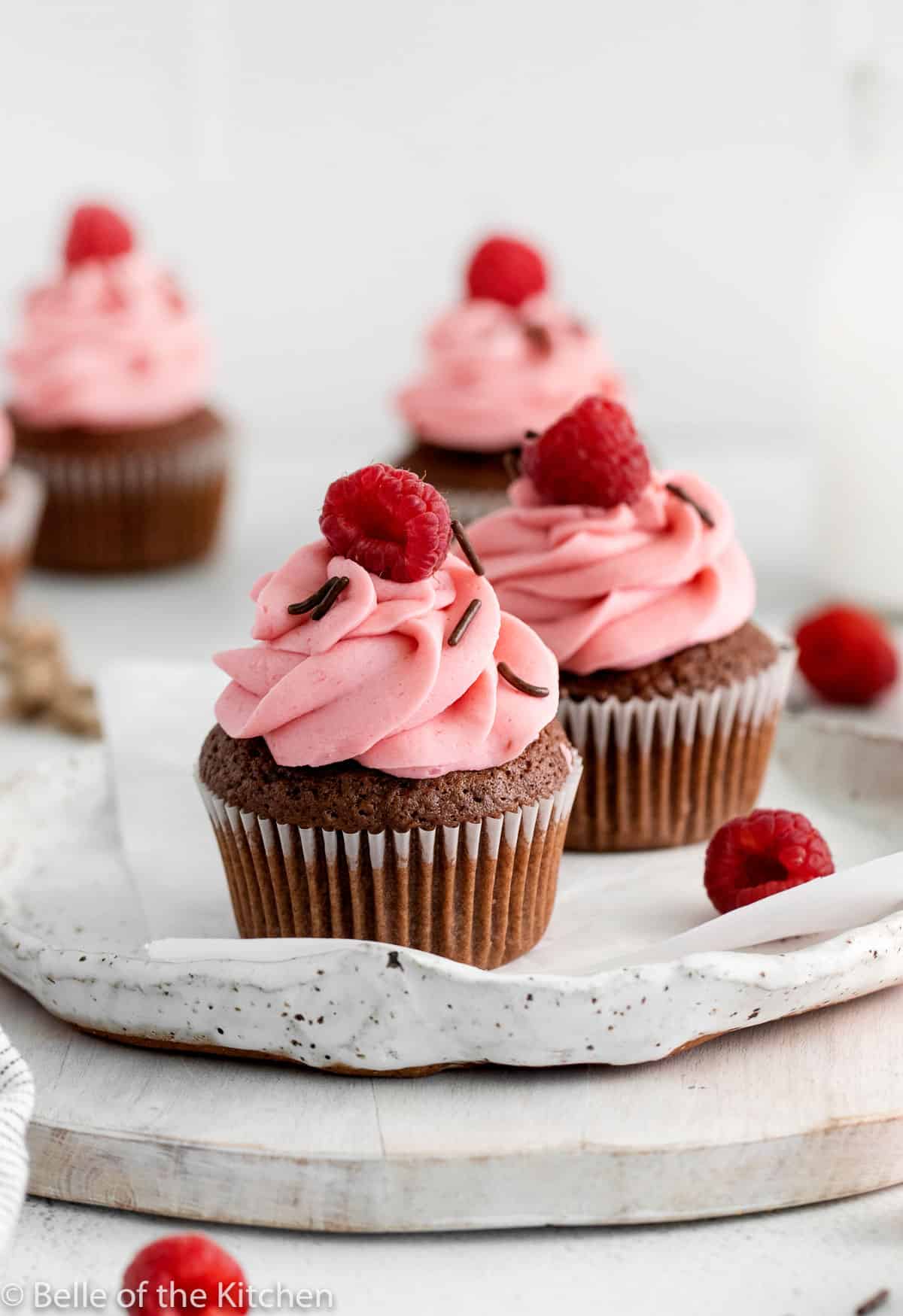 two cupcakes on a plate with raspberries on top.