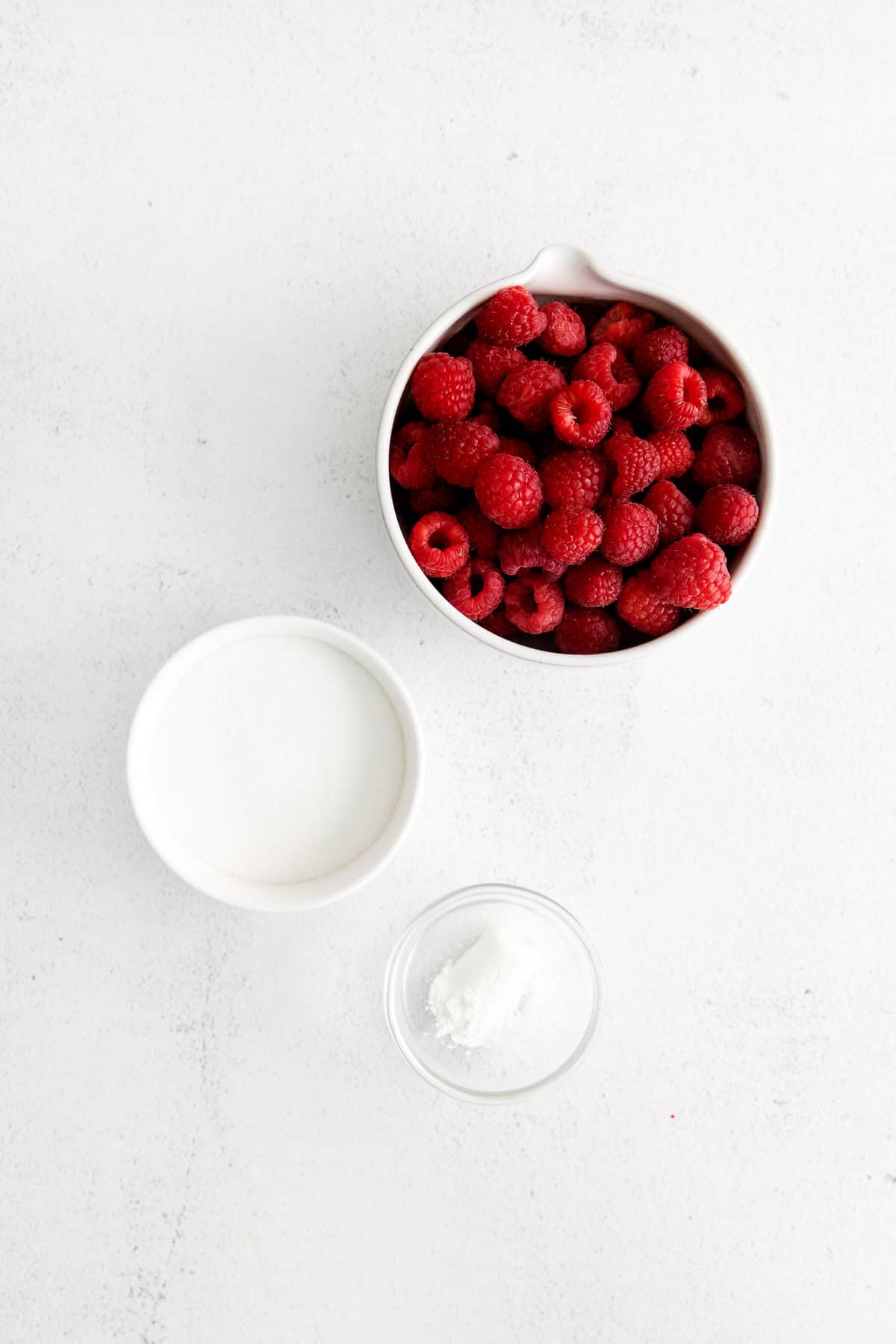 bowls on a counter top with raspberries and sugar.