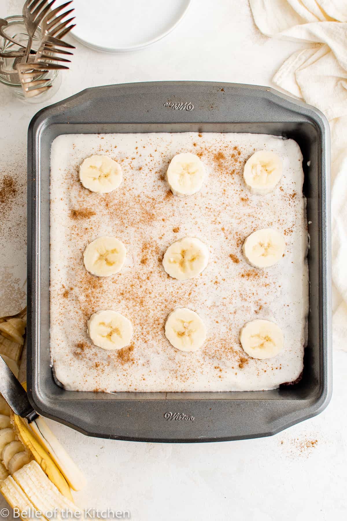 a cake in a metal baking pan topped with vanilla frosting and sliced bananas.