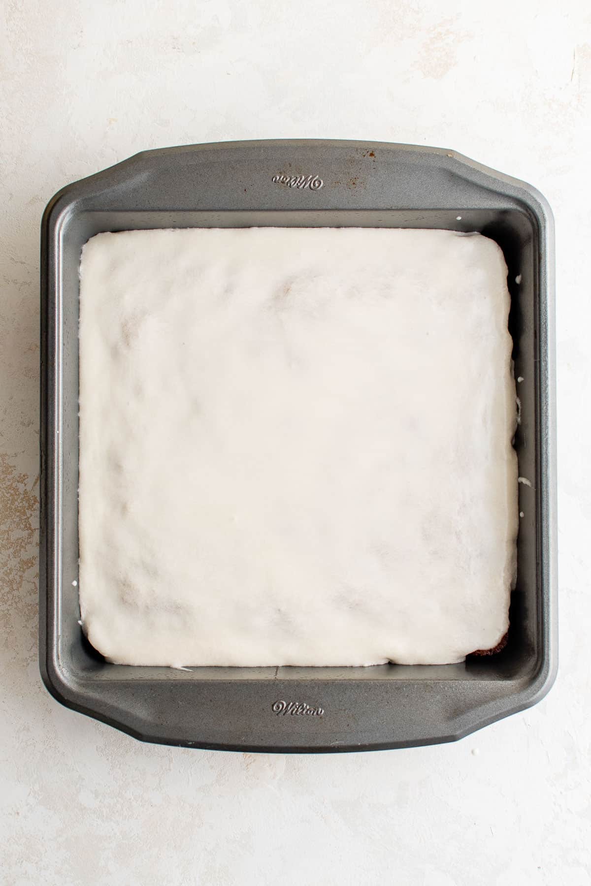 a cake in a metal baking pan topped with vanilla frosting.