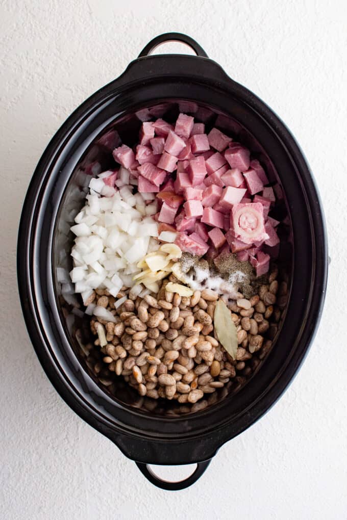 a crockpot bowl full of ham, onions, and beans.