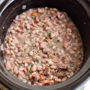 a crockpot bowl full of cooked ham and beans.