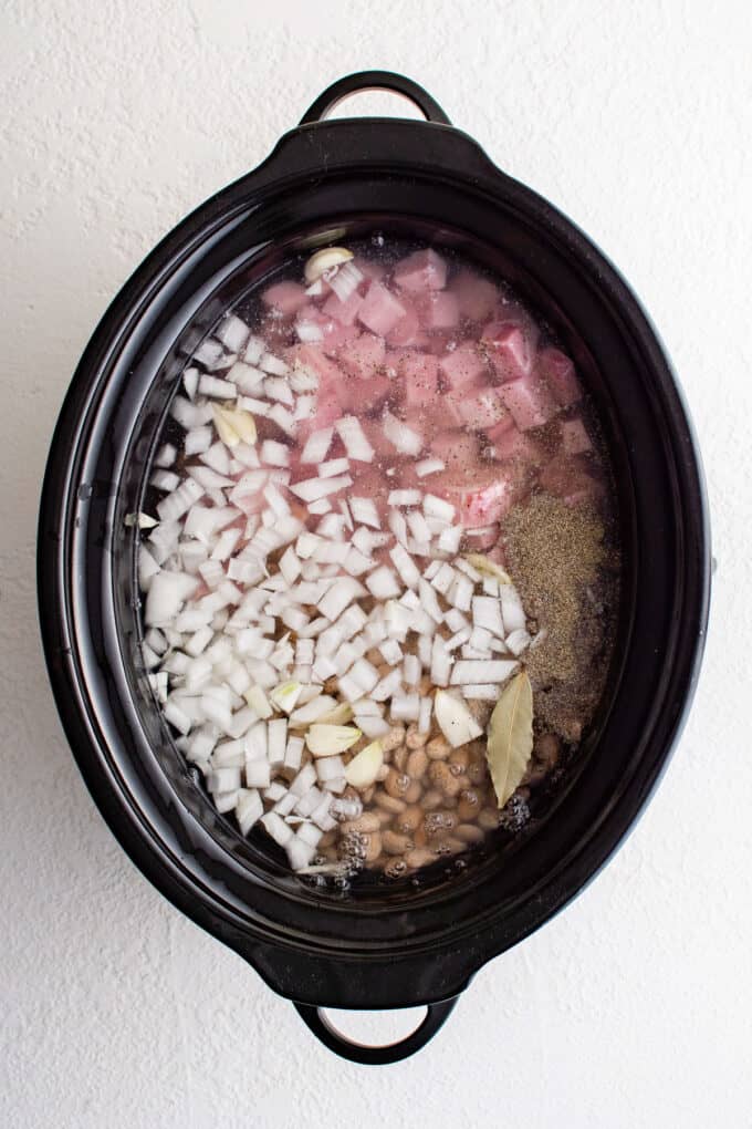 a crockpot bowl full of ham, onions, and beans.