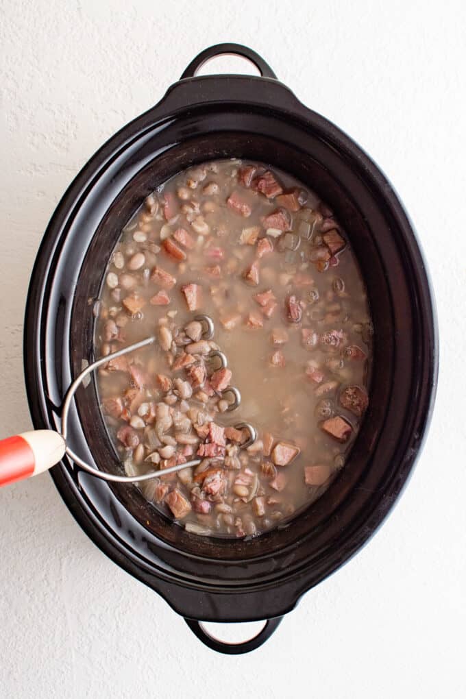 a potato masher mashing beans in a crockpot.