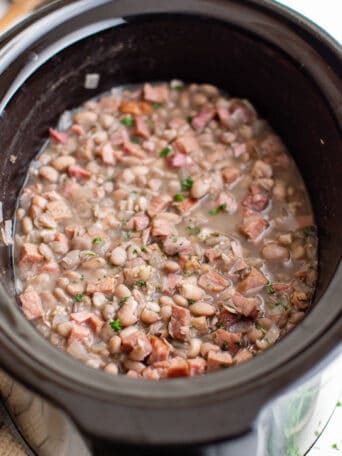 a crockpot bowl full of cooked ham and beans.
